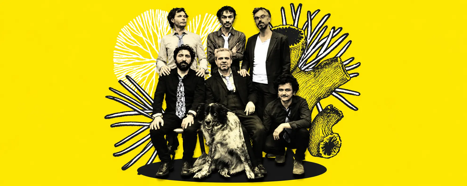 Band photo six men with a large dog posed on a black platform against a bright yellow backdrop with black abstract drawings