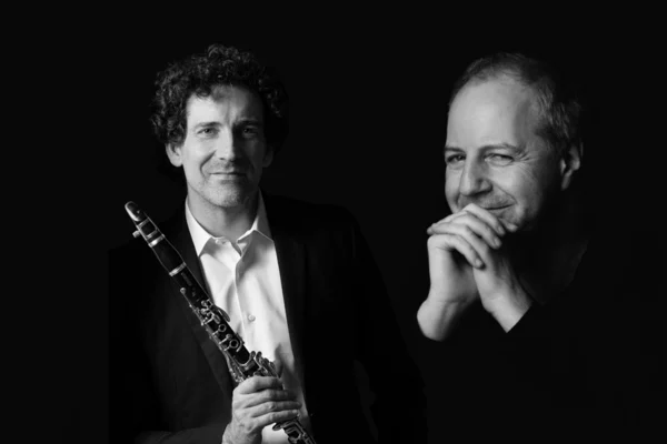 Two male musicians in black-and-white, one holding a clarinet, posed against a dark background.
